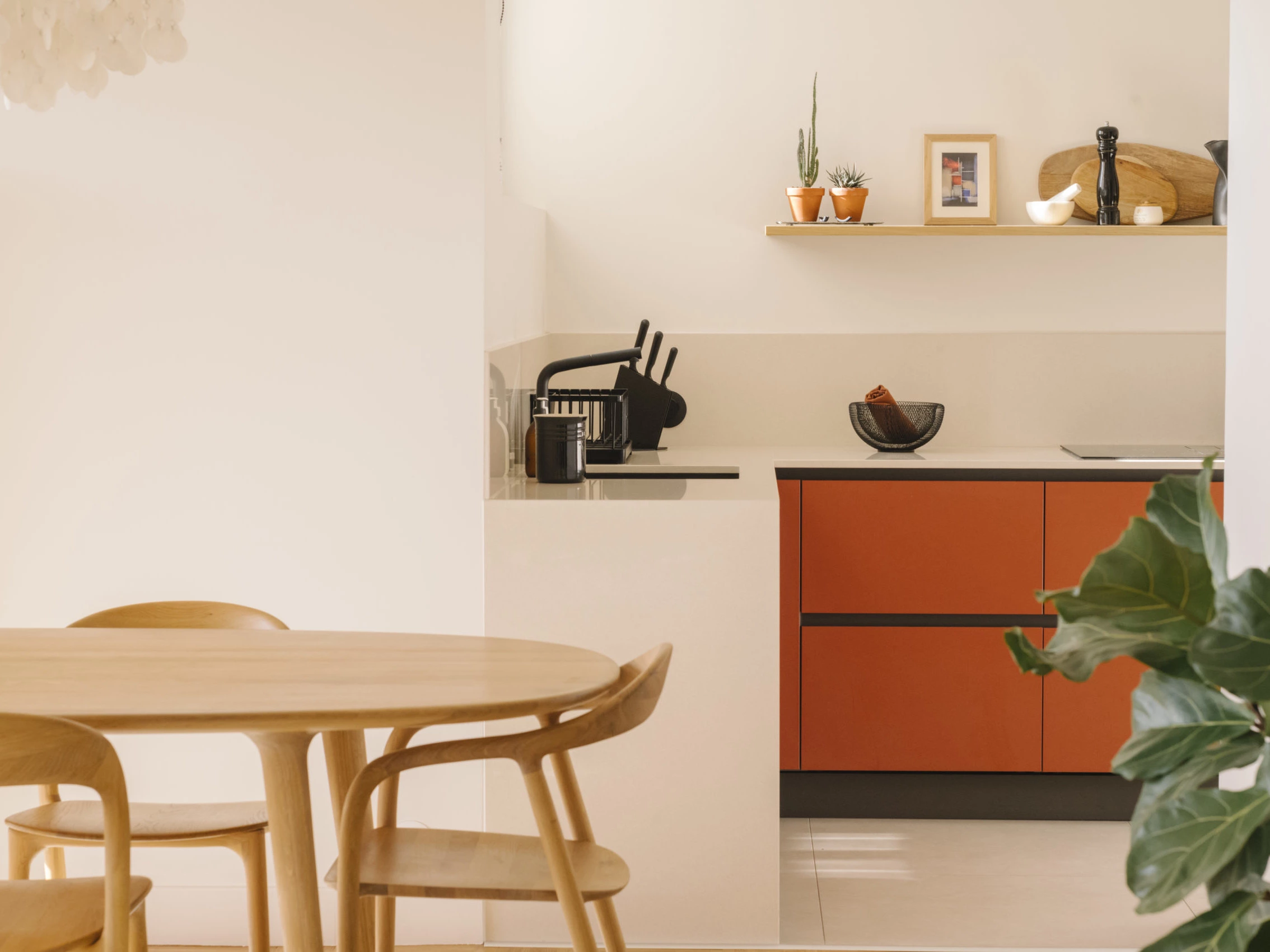 Cuisine ouverte : meubles bas terracotta, table ronde en chêne et étagère en bois