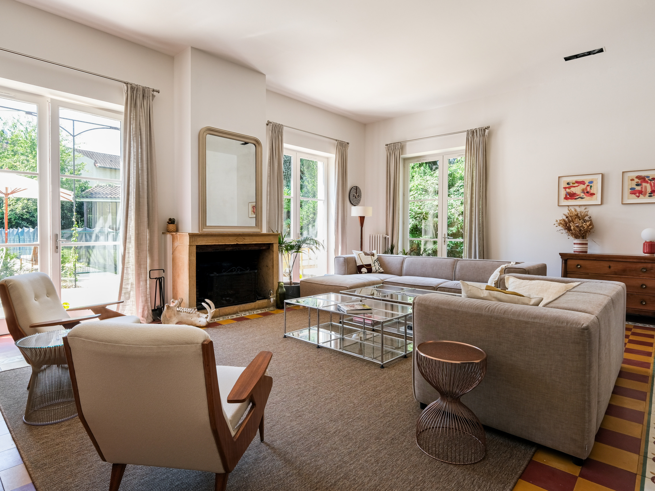 Séjour familial avec cheminée, miroir, canapés gris et guéridon Platner, sol tomettes et baies sur jardin, ESQUI STUDIO