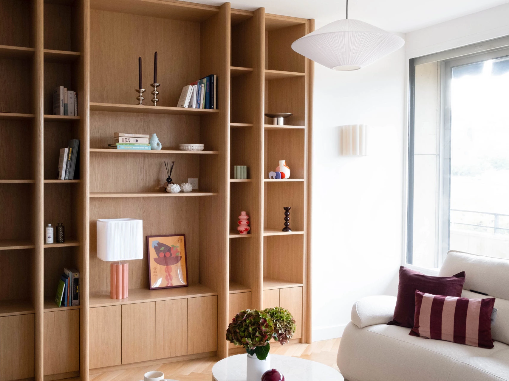 Séjour avec bibliothèque sur-mesure en chêne, canapé écru, tables basses organiques en travertin et suspensions en papier, appartement rénové à Lyon